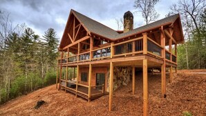 A wooden cabin with a stone chimney, a balcony, and a view of the surrounding forest. - Luxury Mountain Cabin with Amazing Views and Hot Tub (Dog Friendly) (Blue ridge)