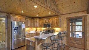 A modern kitchen with wooden cabinetry, stainless steel appliances, and a bar area with stools. - Luxury Mountain Cabin with Amazing Views and Hot Tub (Dog Friendly) (Blue ridge)