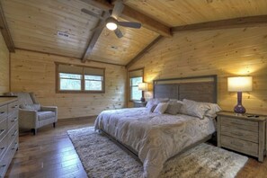 Quarto de cabana de madeira com cama, mesas de cabeceira, uma cadeira e um ventilador de teto.