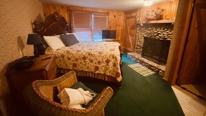 Ein gemütliches Schlafzimmer mit einem hölzernen Bett, einem Nachttisch, einem Korbstuhl, einem Kamin und einem grünen Teppich.