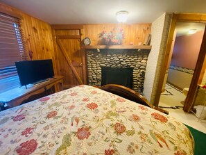 A room with a bed, a television, a stone fireplace, and wooden walls.
