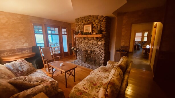 Ein gemütliches Wohnzimmer mit Kamin aus Stein, Sofas mit Blumenmuster und einem Holztisch.