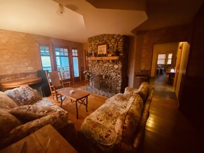 A cozy living room with a stone fireplace, floral-patterned sofas, and a wooden coffee table.