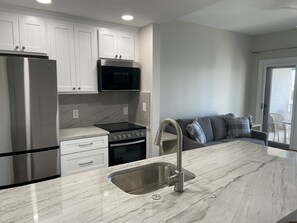 Cozinha moderna com armários brancos, eletrodomésticos de aço inoxidável e bancada de mármore.