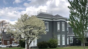 Un bâtiment à deux étages, doté d’une façade sombre et de bordures blanches, entouré d’une pelouse bien entretenue et d’arbres.