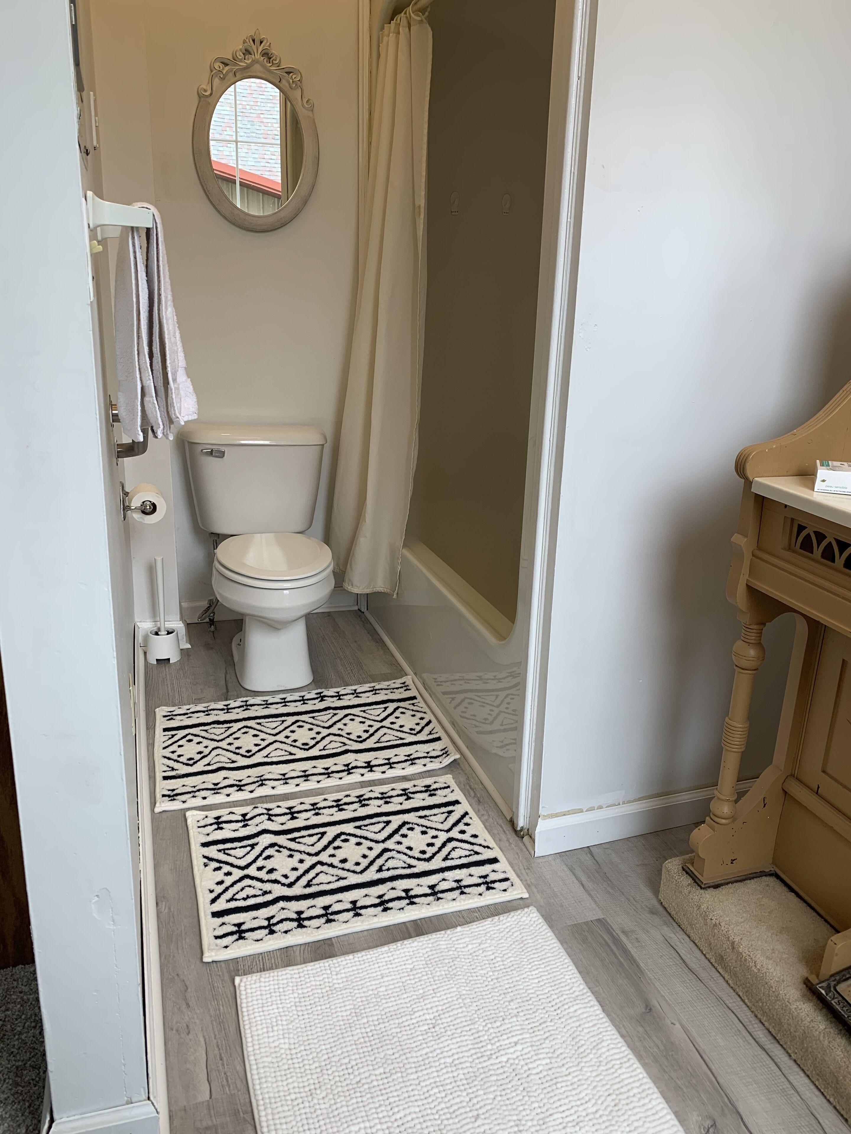 A bathroom with a toilet, a shower curtain, a mirror, and patterned rugs on the floor.