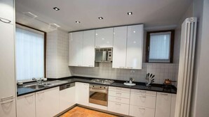 Una cocina moderna con armarios blancos, encimera negra, horno empotrado y una ventana con persianas.
