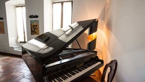 Un piano de cola en una habitación luminosa, con una silla, un cuadro en la pared y una ventana con cortinas.