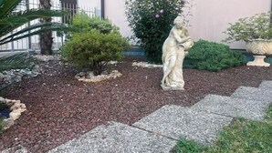 Un jardín con una estatua, una palmera y un edificio con contraventanas.