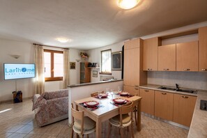 Cozy living space with a dining area and kitchenette, featuring a sofa, dining table for four, flat-screen TV, and kitchenette with sink.