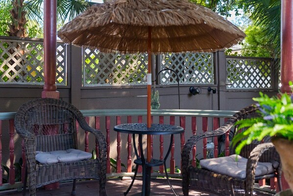 A patio with wicker furniture, a round table, and a thatched umbrella.