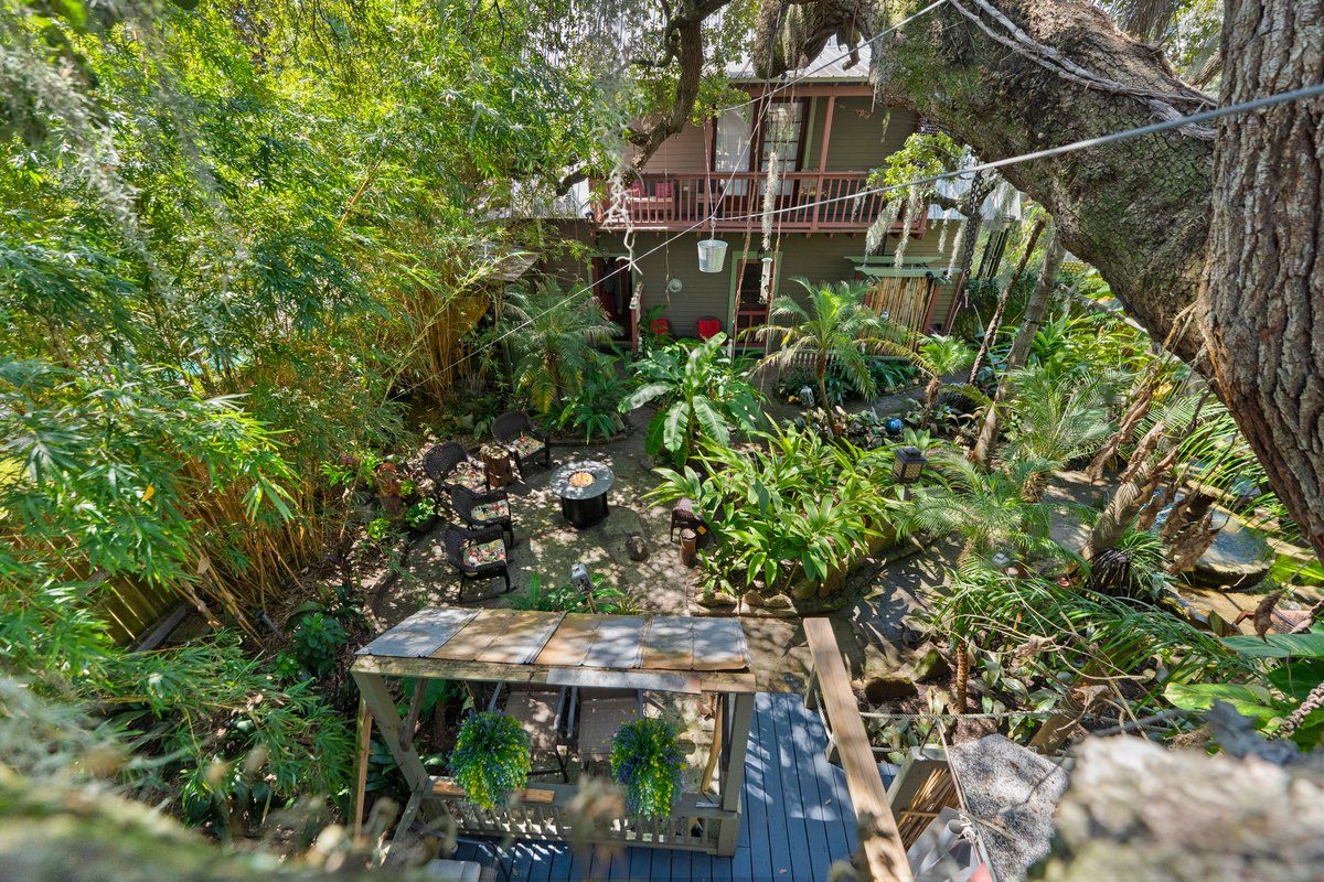 Ein üppiger Garten mit einer Holterrasse, einem kleinen Tisch und einem Haus im Hintergrund.
