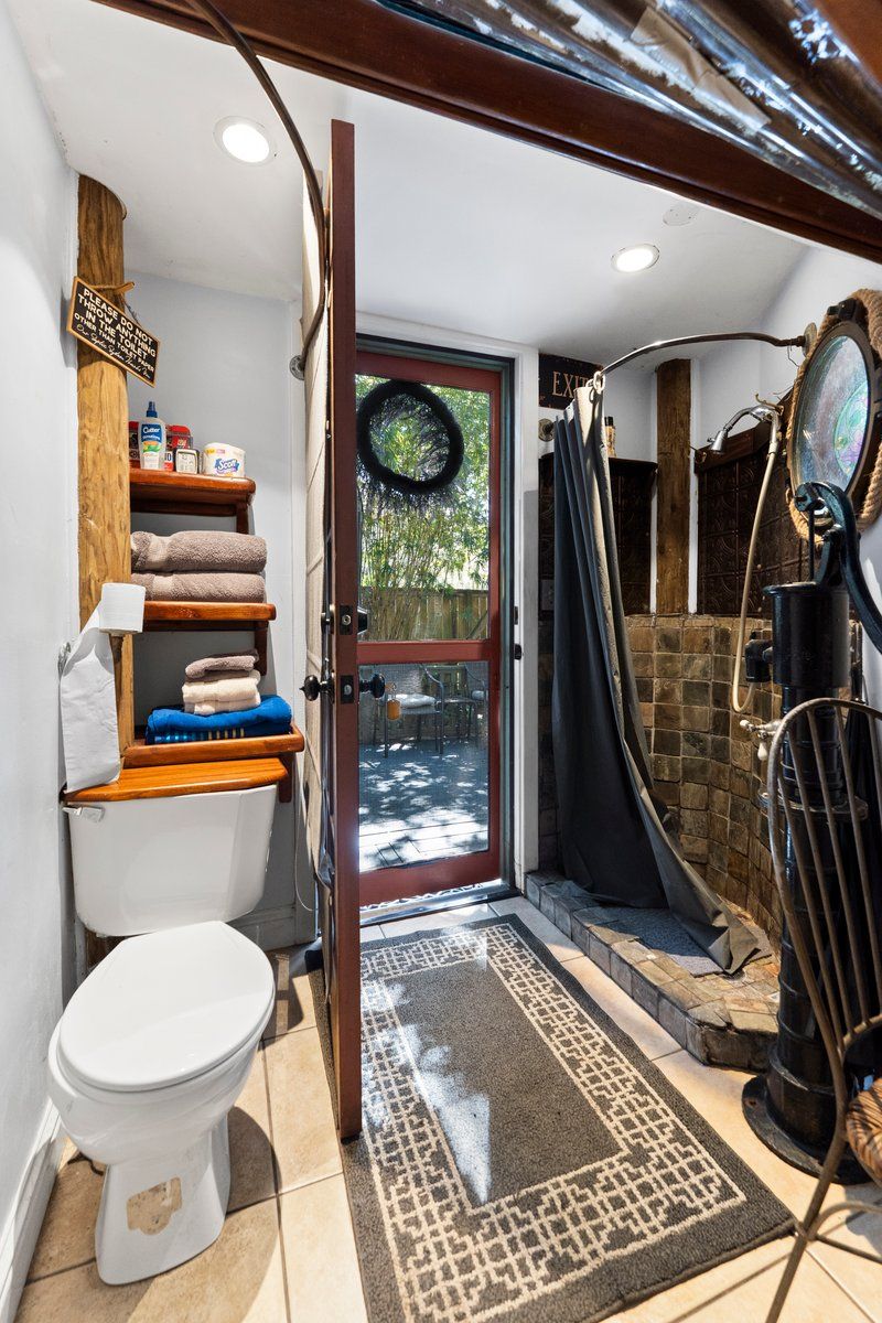A compact bathroom with a toilet, shelves with towels, a shower area, and a visible door leading to an outdoor space.