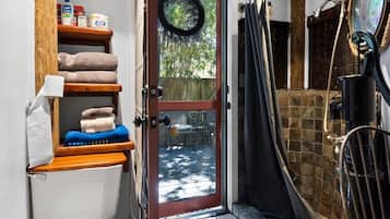 A compact bathroom with a toilet, shelves with towels, a shower area, and a visible door leading to an outdoor space.