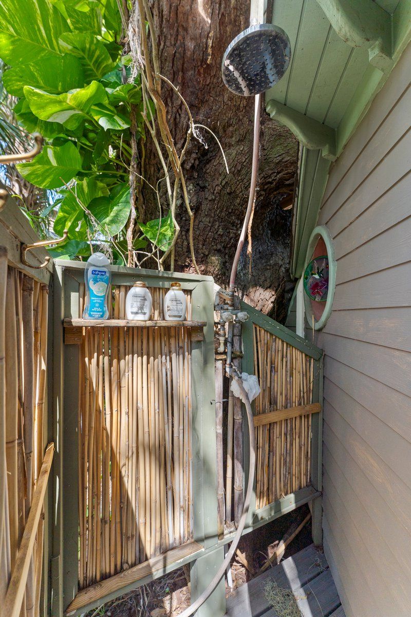 A wooden fence with a bamboo gate, a metal birdbath, and a shelf with bottles.