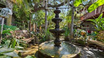A garden with a central fountain surrounded by lush greenery and a wooden deck.