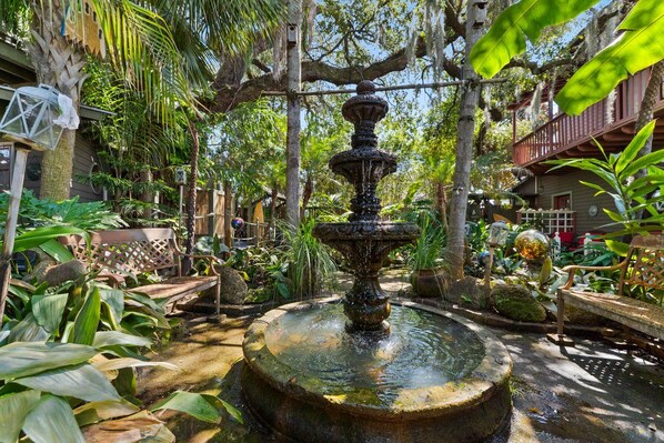 A garden with a central fountain surrounded by lush greenery and a wooden deck.