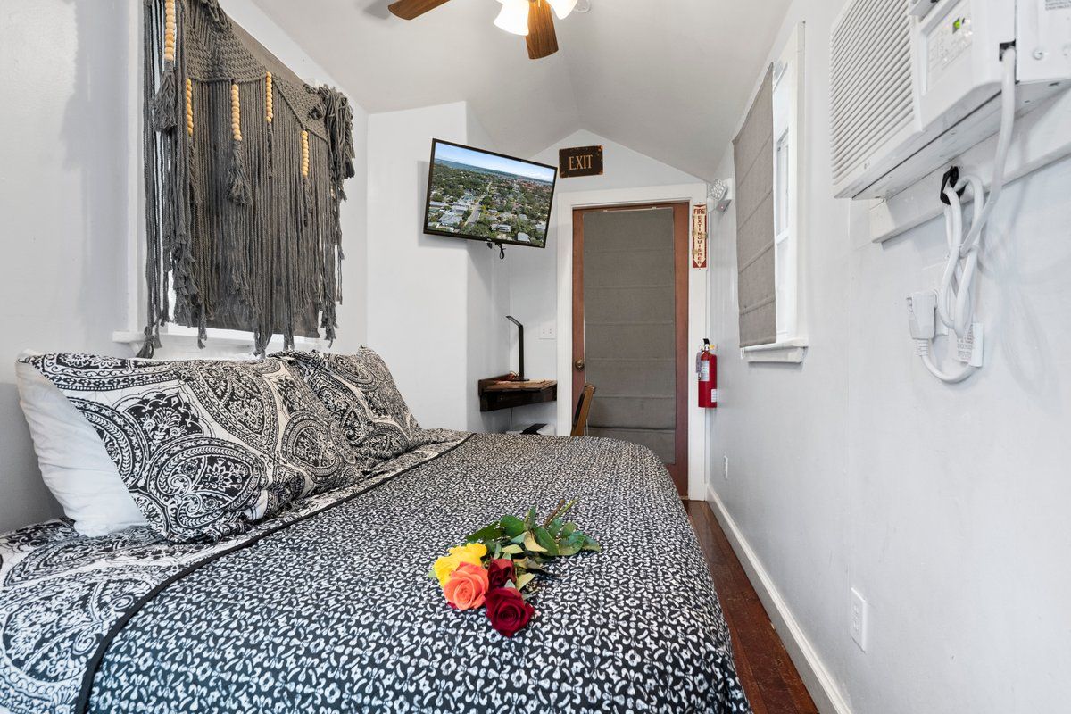 Ein Schlafzimmer mit einem Bett, einem Fernseher, einer Wanddekoration aus Makramee und einer Tür mit einem Ausgangsschild.