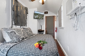 A bedroom with a bed, a television, a wall-mounted macrame piece, and a door with an exit sign.
