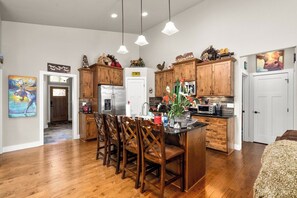 A modern kitchen with wooden cabinets, a central island with chairs, and pendant lighting.