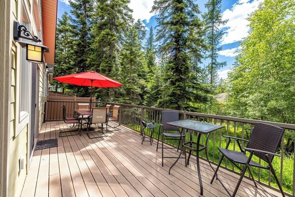 A wooden deck with outdoor furniture, including a table and chairs, and a red umbrella.