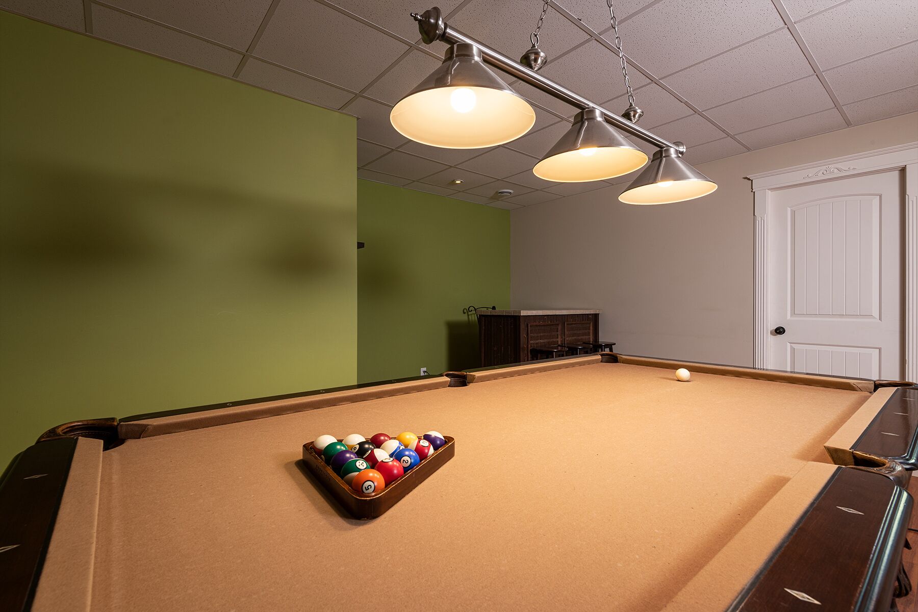 A pool table with balls, a green wall, and a door.