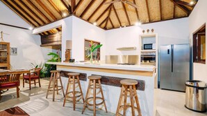 A modern kitchen with a bar area, wooden stools, and a stainless steel refrigerator. - Villa Cira (Seminyak)