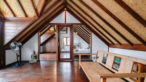 An attic bedroom with wooden beams, a wooden bench, a fan, and a Buddha statue. - Villa Cira (Seminyak)
