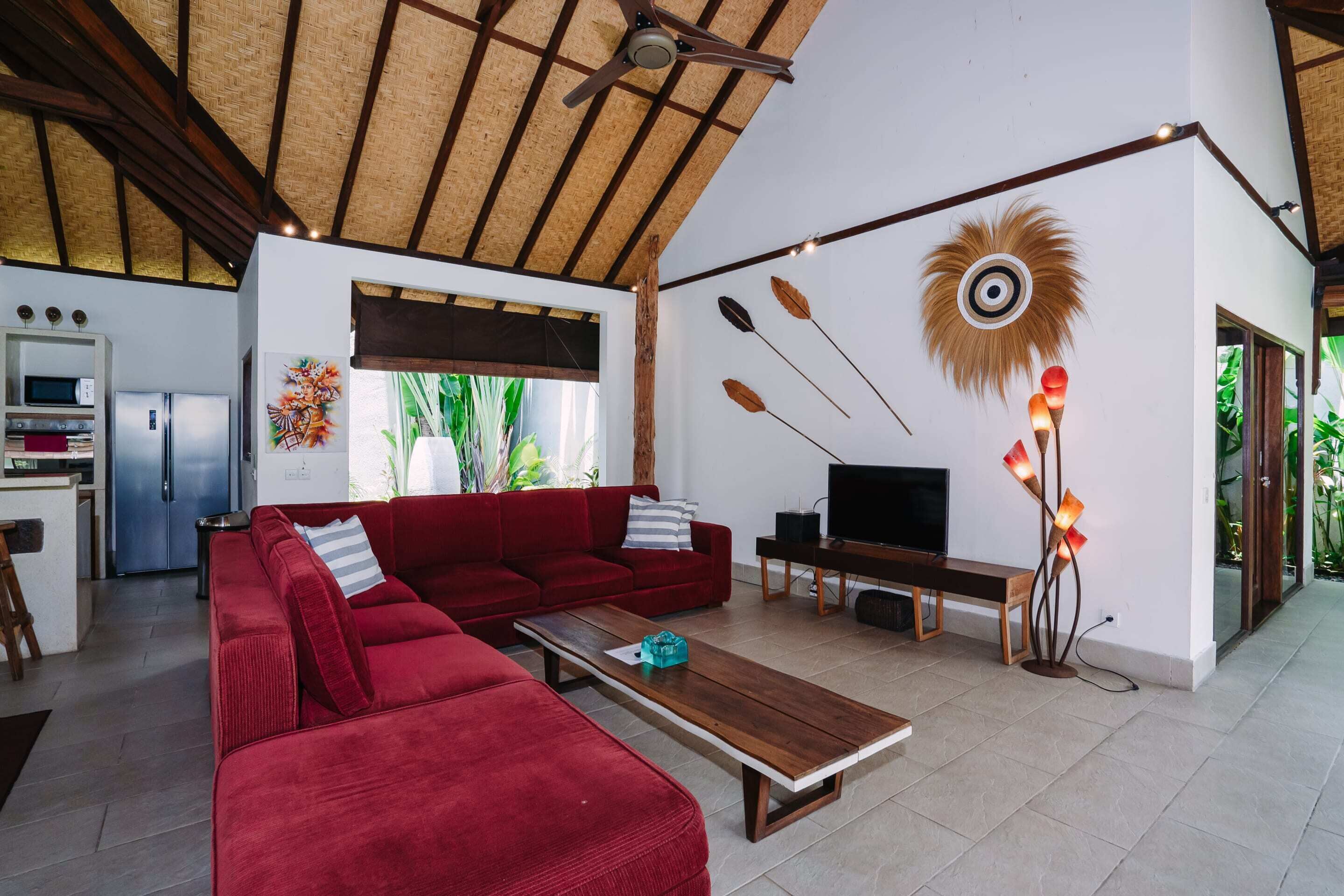 Una sala de estar moderna con un sofá rojo, una mesa de centro de madera y un televisor. Cuenta con una zona de cocina con nevera y microondas, además de una mesa de comedor con sillas.