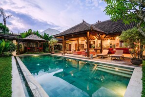 A swimming pool with a covered patio area, a dining space, and lush greenery. - Villa Cira (Seminyak)