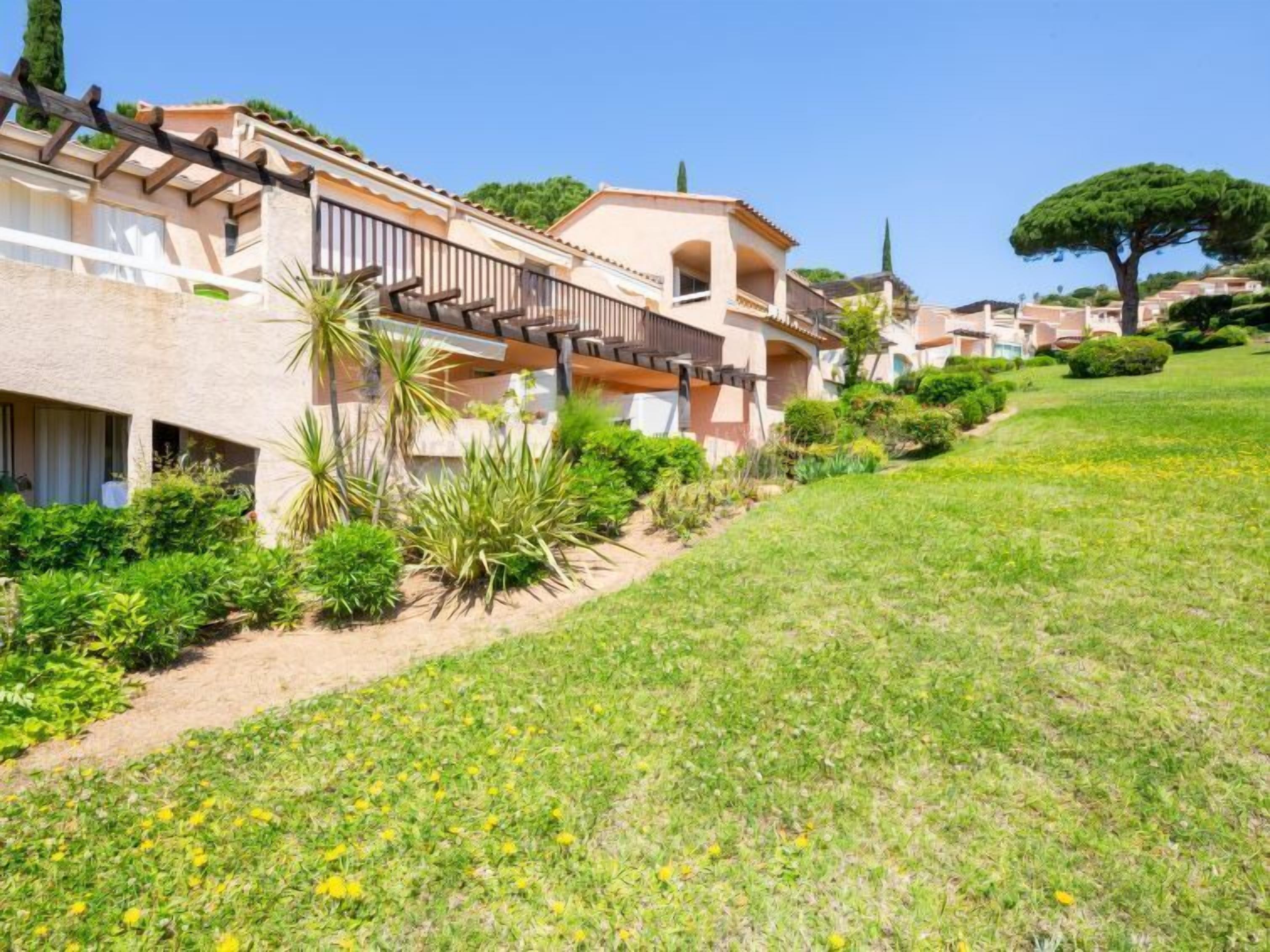 Un edificio residencial con jardín, pérgola y un árbol.