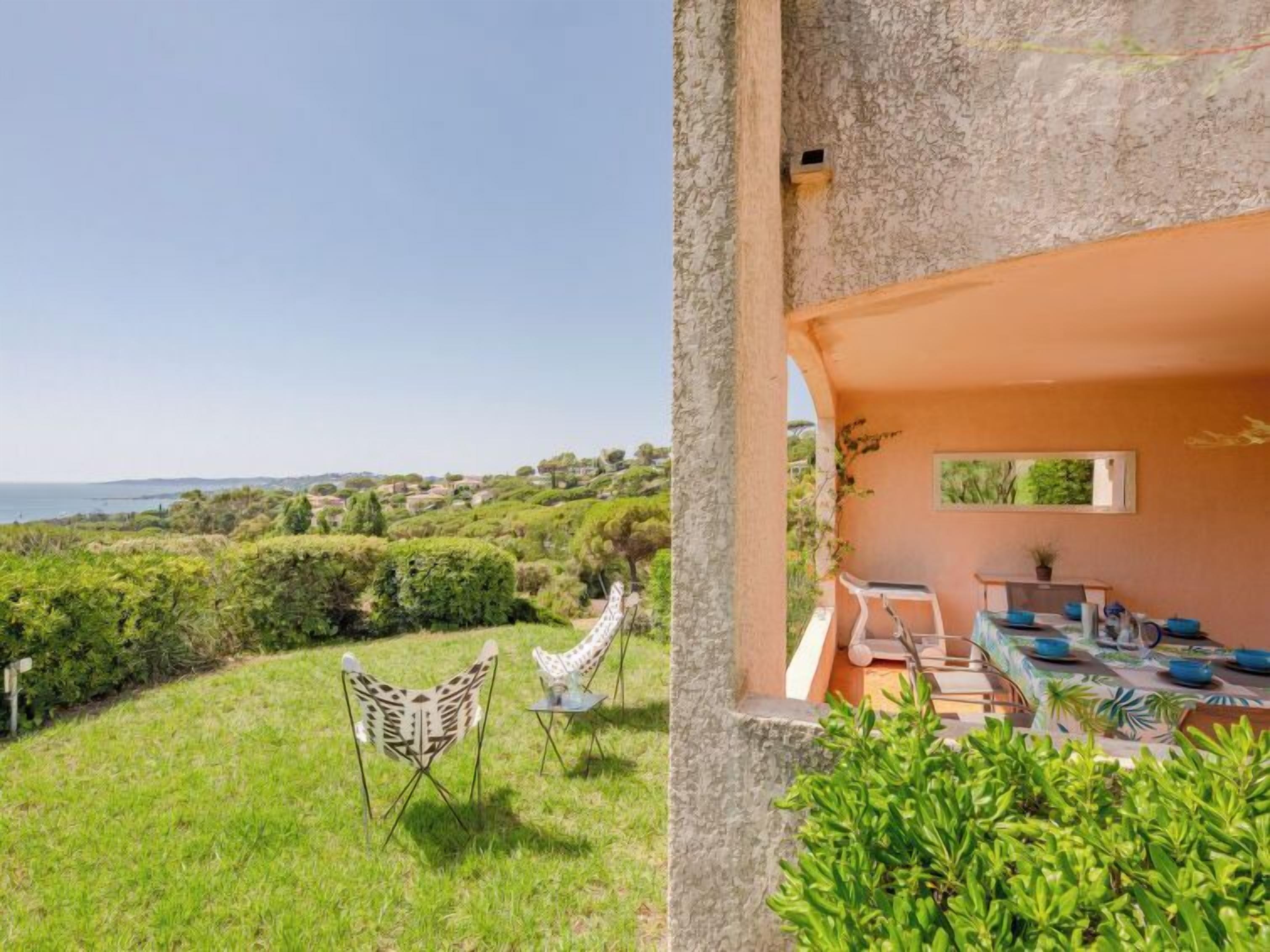 A terrace with a view of the sea, a dining area with a table and chairs, and a garden with a chair.