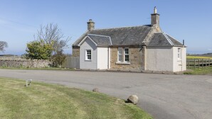 Une maison en pierre à deux étages, avec un toit à pignon, une cheminée et un petit porche à l’avant.
