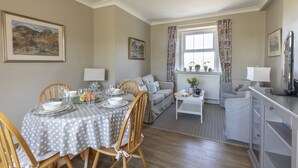 Un coin repas avec une table dressée pour quatre personnes, un canapé, une petite table d’appoint et un radiateur agrémenté de fleurs.