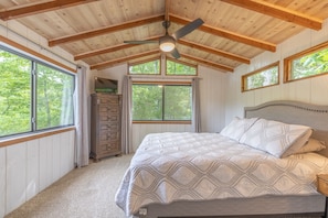 A bedroom with a large bed, a ceiling fan, and windows with curtains.