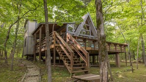Eine Holzhütte mit Treppe und einer Terrasse, umgeben von Bäumen.