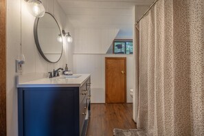 A bathroom with a large mirror, a sink with a blue cabinet, a wooden door, and a patterned curtain. - The Innsbrook Oasis Pt. III by Innsbrook Vacations! (Wright City)