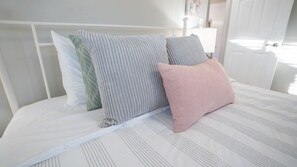 Ein Bett mit einem weißen Kopfteil, einem gestreiften Kopfkissen und einem rosafarbenen Kopfkissen.