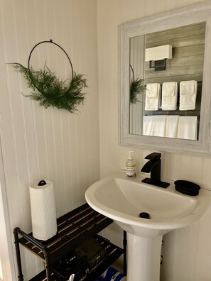 Ein Badezimmer mit einem weißen Waschbecken, einem Spiegel und einem Handtuchhalter mit drei Handtüchern.