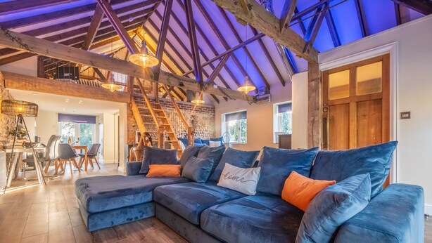 A spacious living area with a large sectional sofa, wooden flooring, and a high ceiling with exposed beams. - Homestead and Black Cat Barn, Southrepps, Norfolk (Southrepps)