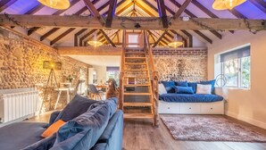 A cozy loft-style room with a wooden staircase, a blue sofa, and a stone wall. - Homestead and Black Cat Barn, Southrepps, Norfolk (Southrepps)