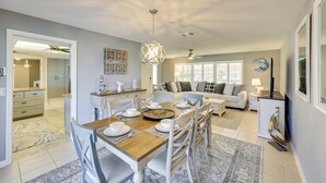 Una cocina moderna con zona de comedor, que presenta una mesa de madera dispuesta para cuatro personas, sillas blancas y una araña.