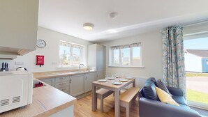 A modern kitchen with a dining area, a sofa, and a window with curtains. - G07 Tweenbanx (G7), Riviere Towans (Hayle)