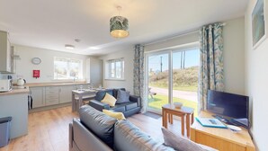 A modern living room with a sofa, a TV, and a dining area with a table and chairs. - G07 Tweenbanx (G7), Riviere Towans (Hayle)