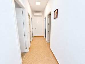 A corridor with white walls, a tiled floor, and doors leading to rooms.