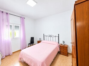 A bedroom with a bed, a nightstand, a chair, a wardrobe, and a window with curtains. - Chalet Garrido with private fenced pool (Conil de la Frontera)
