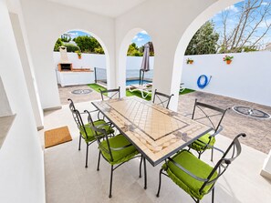 A patio with a tiled table and chairs, a barbecue grill, and a pool in the background. - Chalet Garrido with private fenced pool (Conil de la Frontera)