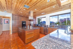 A modern kitchen with wooden ceiling, stainless steel appliances, and large windows offering a view of the mountains.