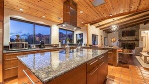 A spacious kitchen with granite countertops, wooden cabinets, and a large island. It features a stone fireplace and a large window overlooking a mountainous landscape. - Spacious Ranch House Sedona  (Sedona)
