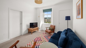 A living room with a sofa, a television, a wooden coffee table, a patterned rug, and a window with a view.